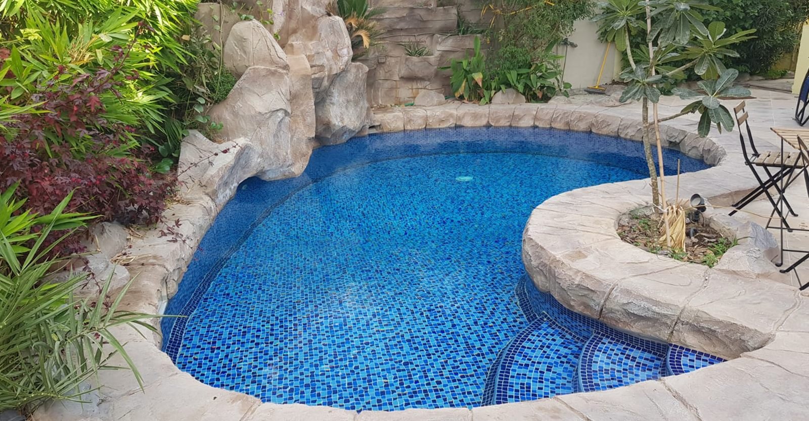 Natural rock-edged mosaic-tiled garden swimming pool